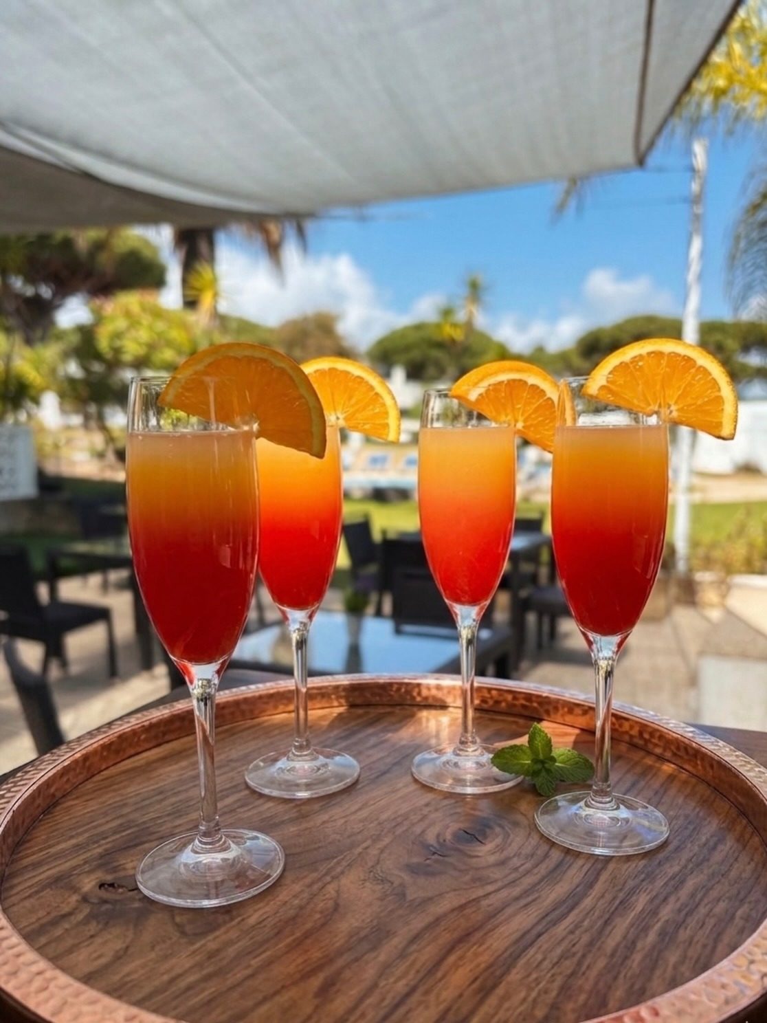 Four sunrise mimosas on a wooden tray under the cafe canopy